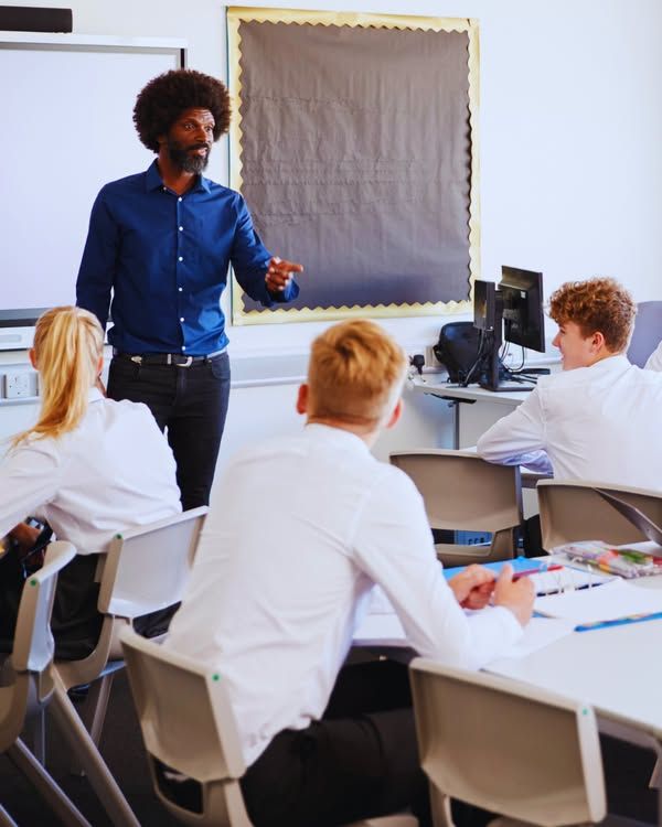 Adult, standing, addressing three teenagers sat at desks